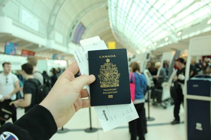 Canadian passport with boarding passes held at a busy airport terminal.