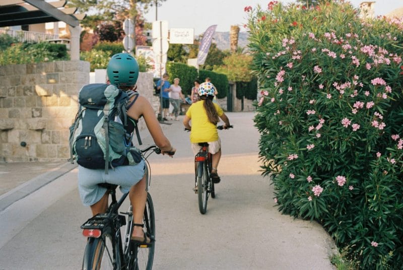 Two people cycling on a scenic path with blooming flowers and greenery.