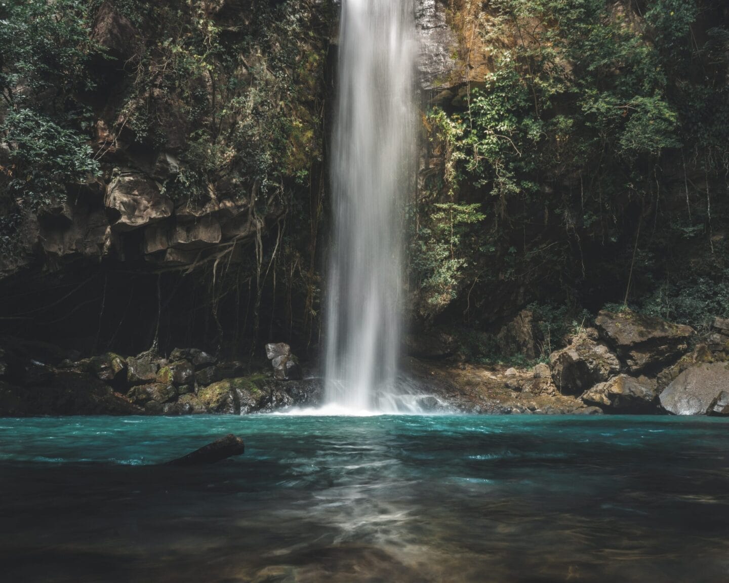 Majestic waterfall cascading into a serene turquoise pool surrounded by lush greenery and rocky cliffs.