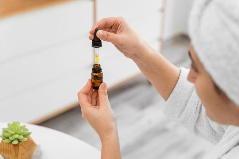 Person holding a glass dropper with essential oil in a relaxing spa setting.