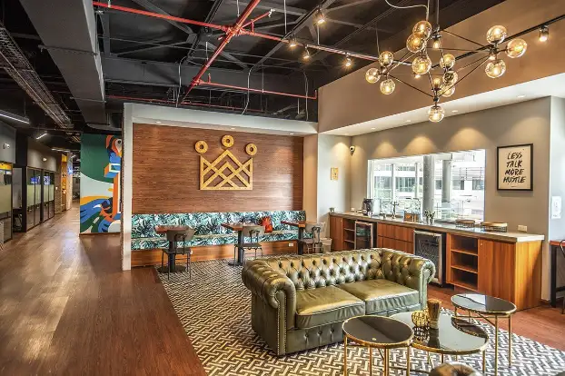 Modern office lounge with leather couch, wooden decor, geometric rug, and stylish lighting for a cozy work environment.