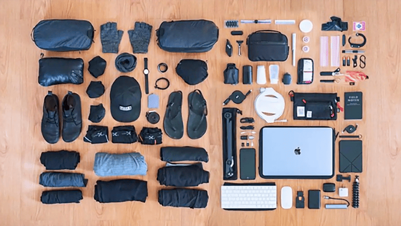 Flat lay of travel essentials including clothes, gadgets, and accessories neatly arranged on a wooden floor.