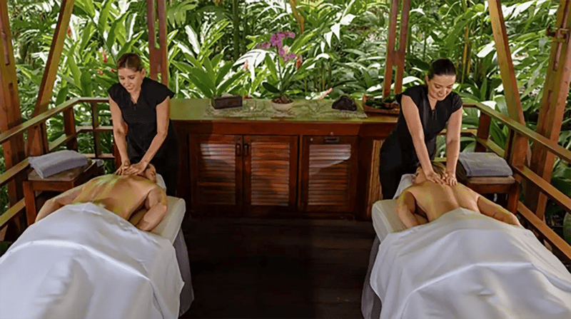 Two people enjoy a relaxing outdoor massage surrounded by lush greenery.